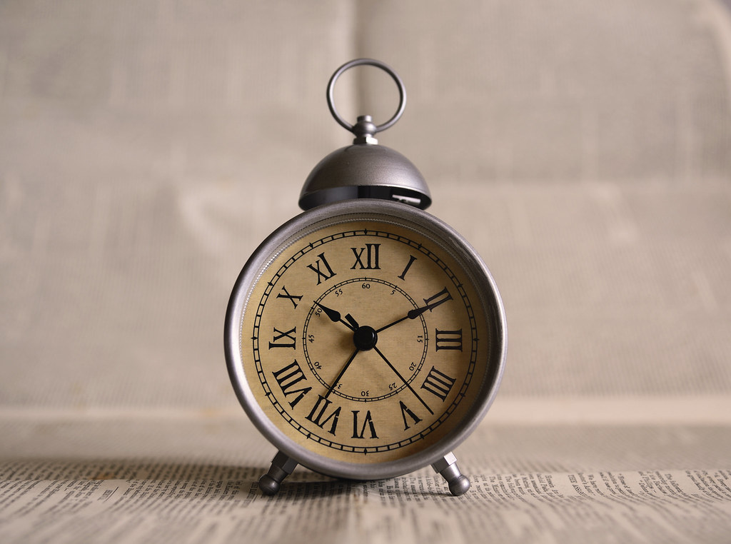 Mesa de trabalho à noite com relógio marcando hora tardia, xícara de café e calendário aberto mostrando o início da semana