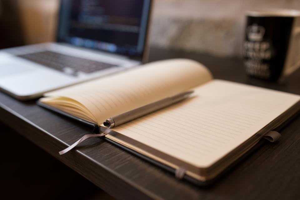 Caderno aberto com caneta e xícara de chá sobre mesa de madeira