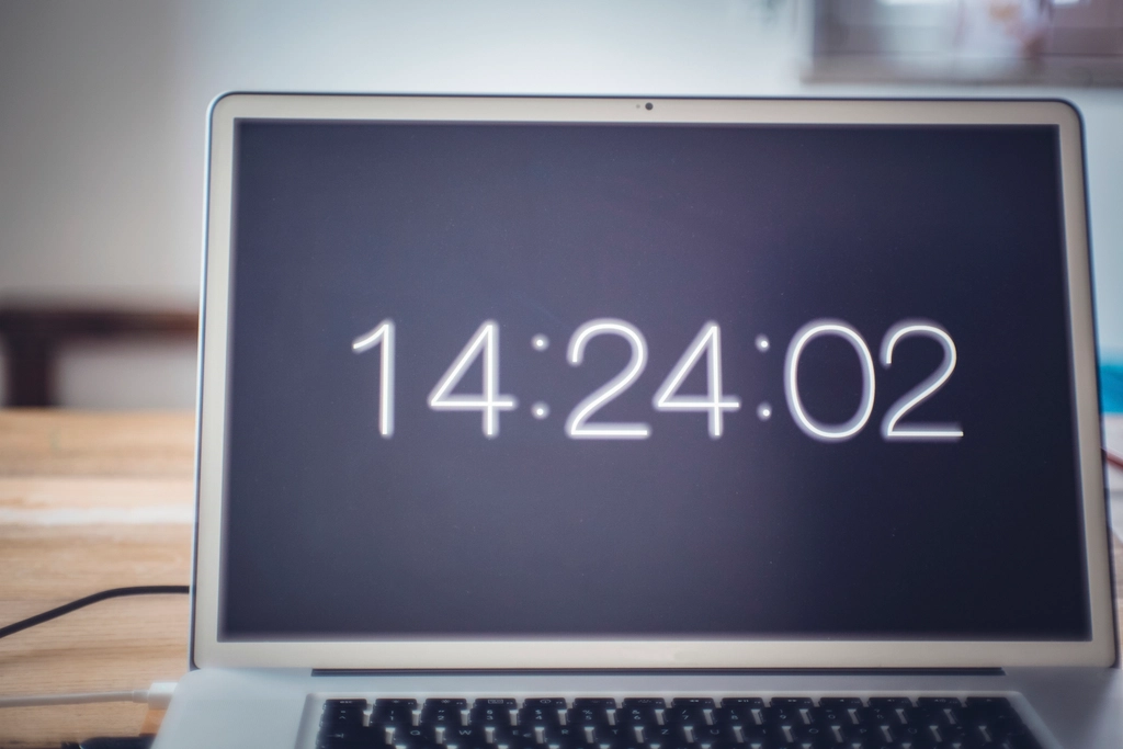 Laptop exibindo horário preciso (14:24:02) ilustra a obsessão por detalhes e controle associada ao perfeccionismo.
