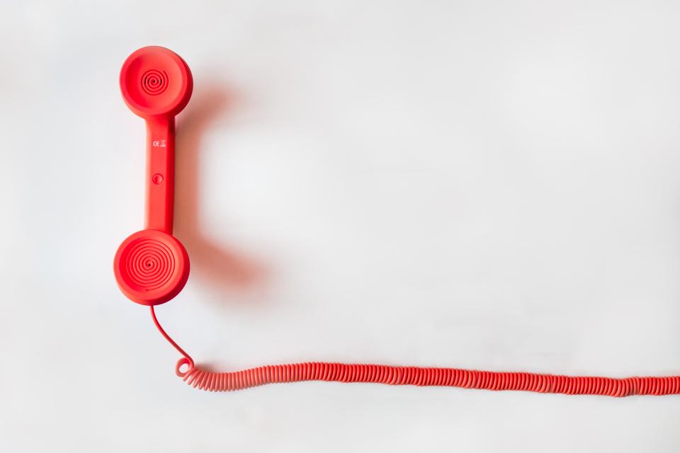 Um telefone vermelho vintage com fio espiral representa a comunicação e a necessidade de estabelecer contato, ilustrando
